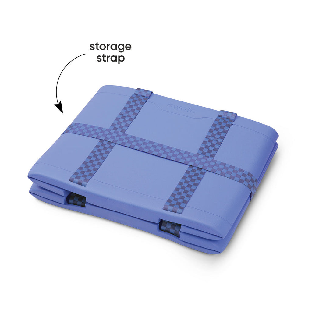 Owala Sun-Day Collapsible Tote in Wavelength shown folded flat with its storage strap secured across the top, periwinkle blue body with blue checker storage strap, with text overlay reading "storage strap"